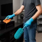 “Person städar biorum med fokus på rena teknikytor, organiserade kablar och dammfria prylar i modern hemmiljö”