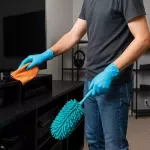 “Person städar biorum med fokus på rena teknikytor, organiserade kablar och dammfria prylar i modern hemmiljö”